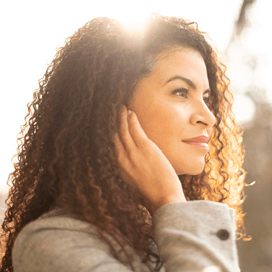 Woman with long brown curly hair with hand on ear