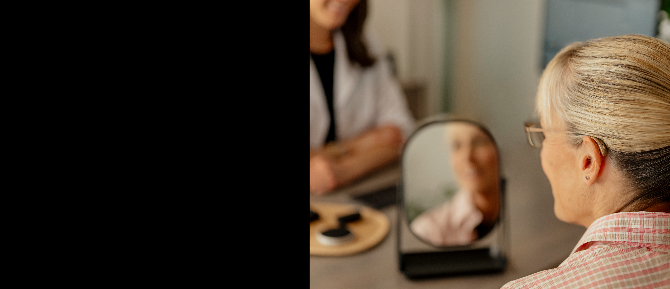 Woman trying on hearing aids smiling in the mirror.