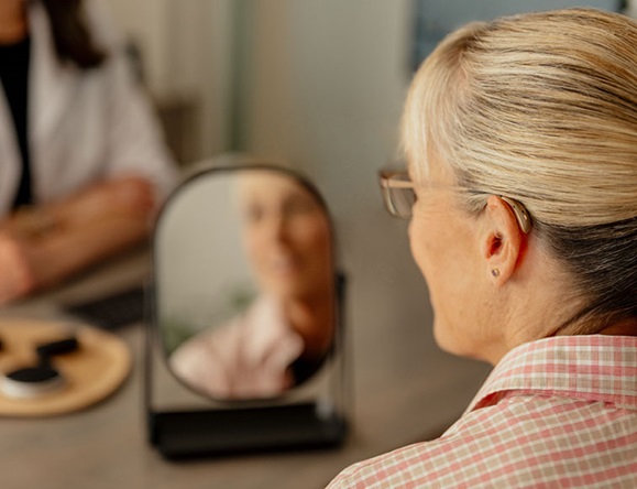 Woman trying on hearing aids smiling in the mirror.